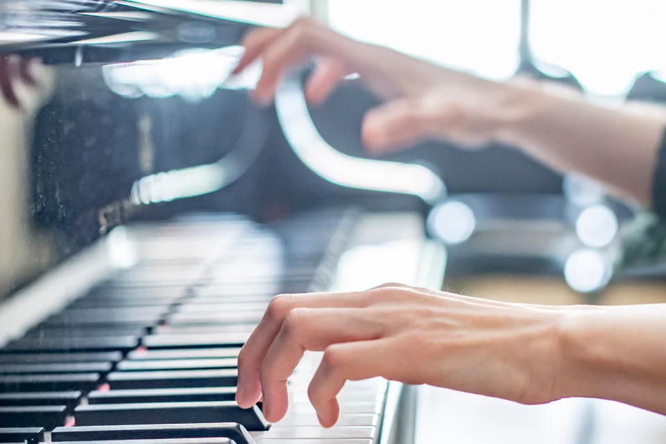 A close up of a piano keyboard with hands playing 