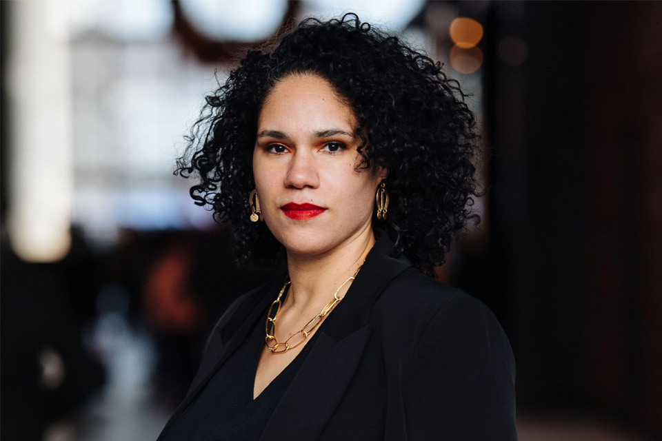 A woman with curly dark hair and bright red lipstick wearing all black looking into the camera