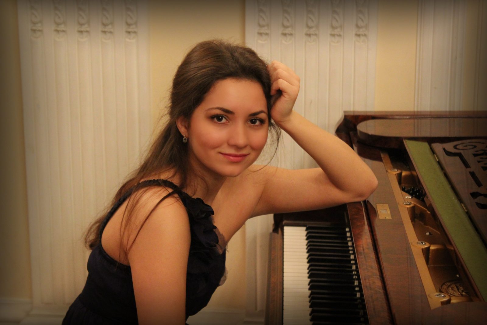 A woman looking into the camera and leaning one elbow on top of a piano
