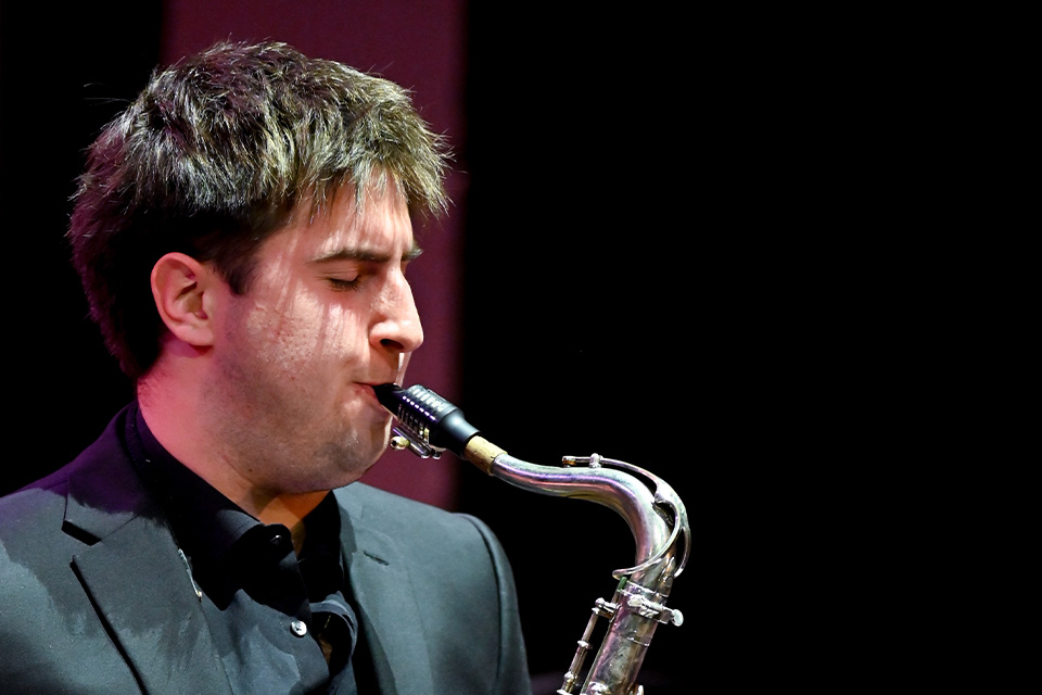 A young man plays the saxophone in a dark room