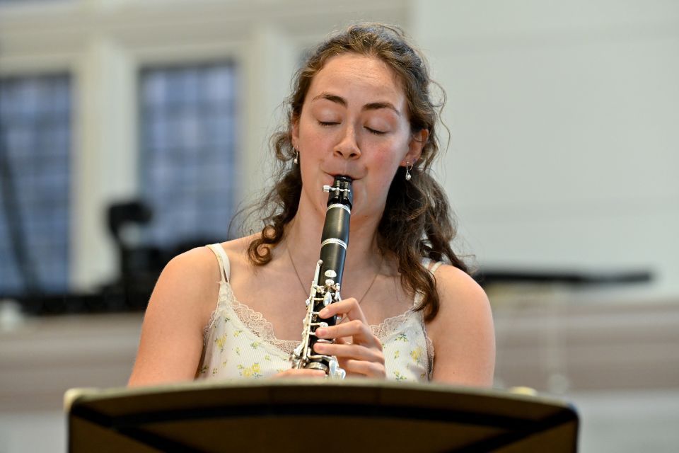 A young woman plays the bassoon in a bright room