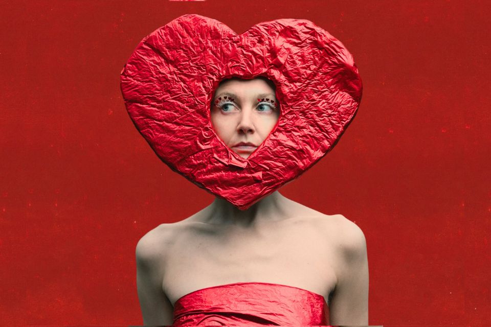 A young woman wears a red heart surrounding her face in front of a red background