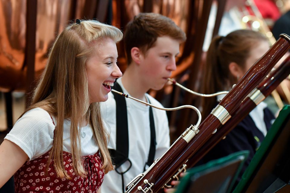 A young woman laughs as she holds a bassoon in an orchestra