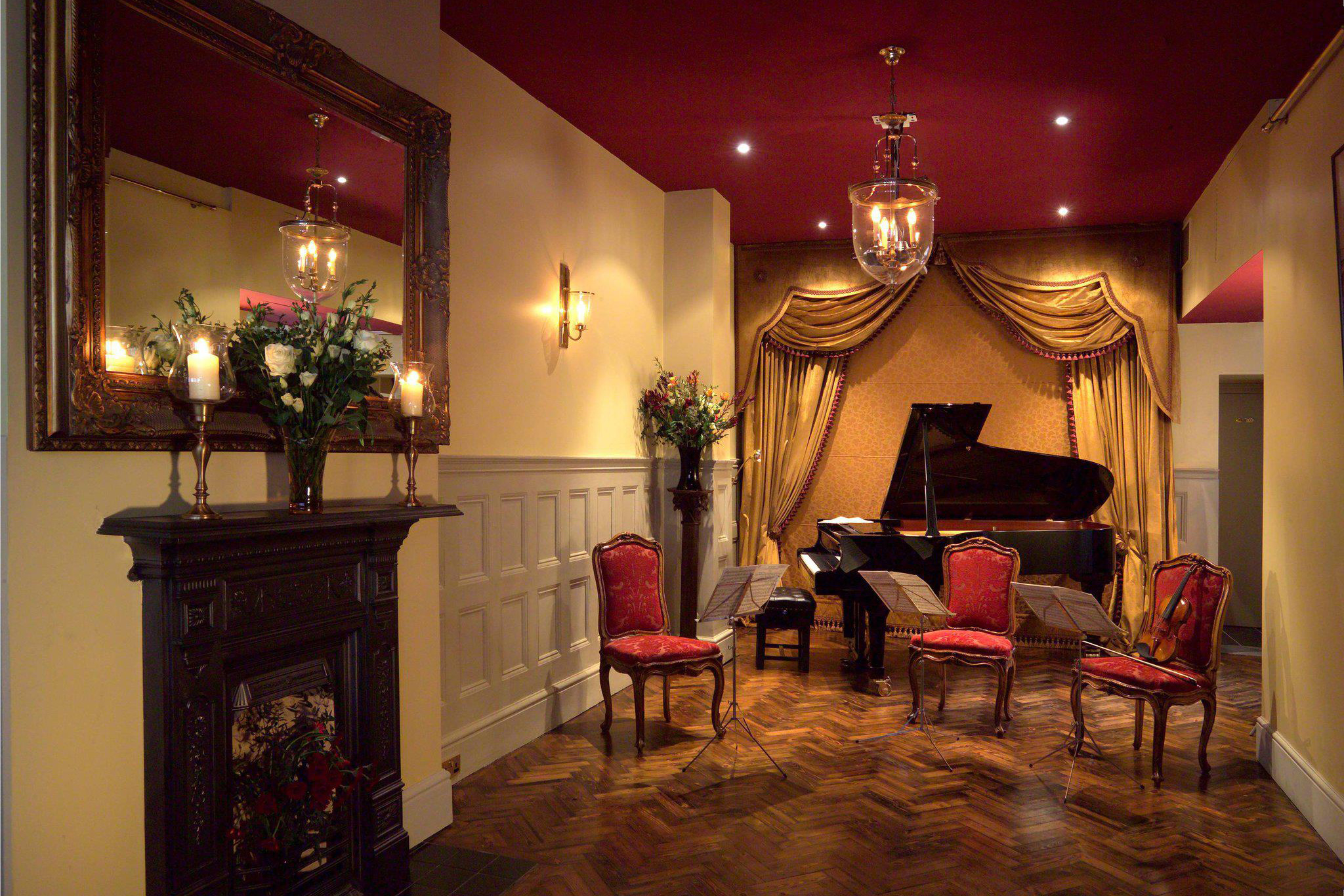 The interior of an ornate room with parquet flooring, red chairs, a mirror on the wall and a grand piano at the back of the room