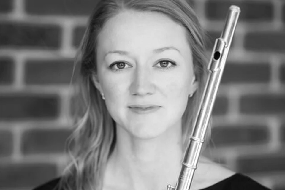 A black and white photo of Amy Yule holding her flute and smiling softly at the camera