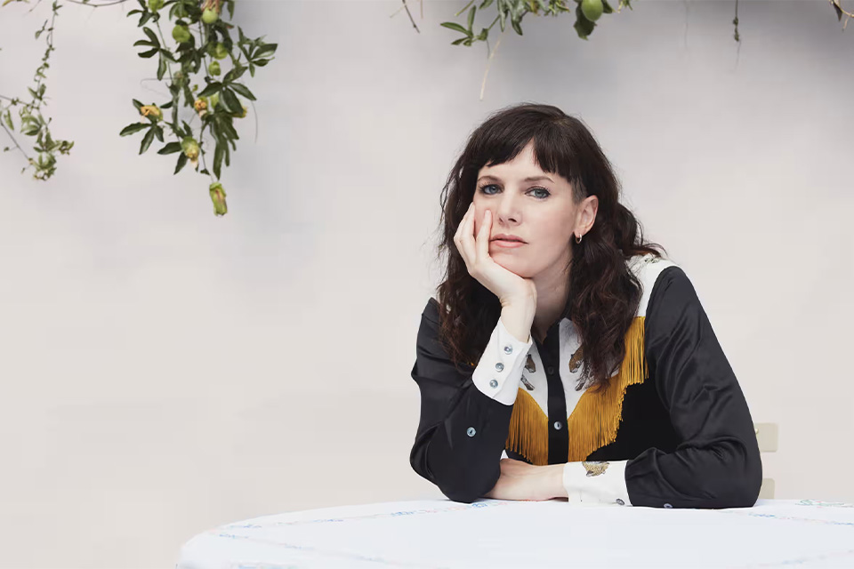 Anna Meredith sits at a table a rests her head on her hand