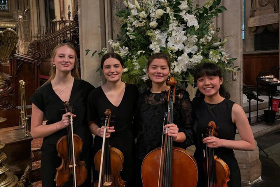 The Apollo Quartet wear all black and hold their instruments, smiling
