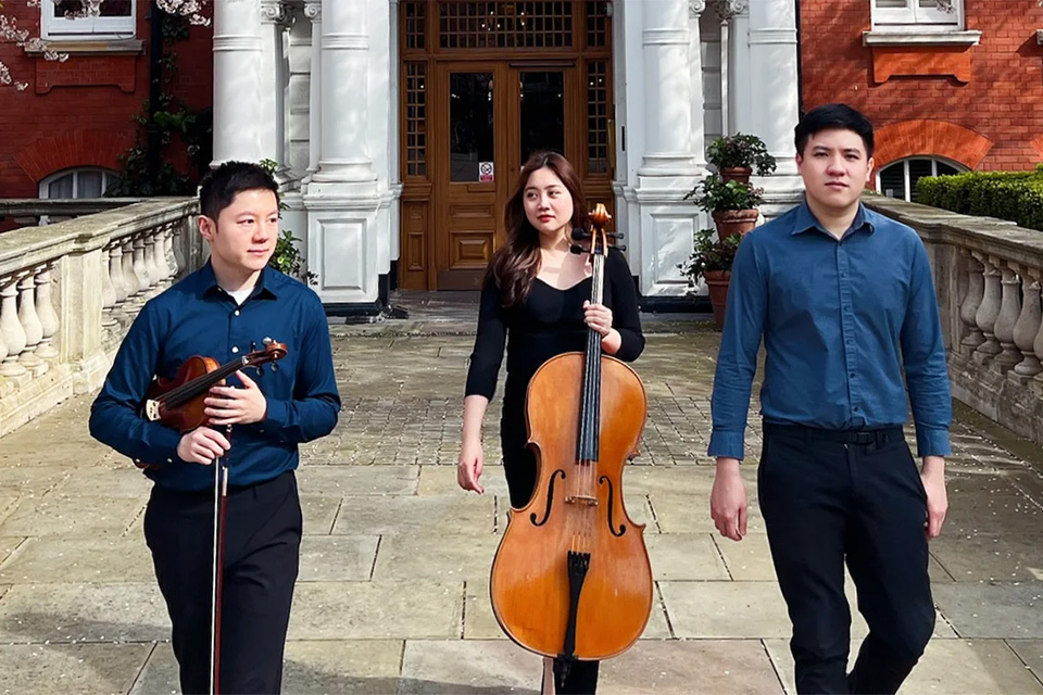 Asterios Piano Trio walk away from a grand building holding their instruments