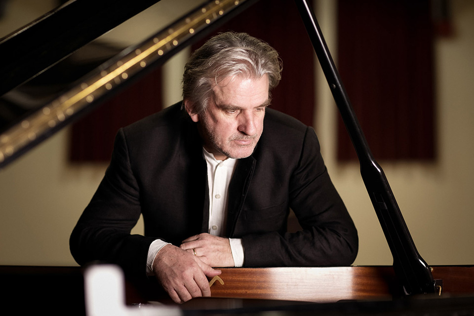 Barry Douglas, wearing a suit, leans on the piano
