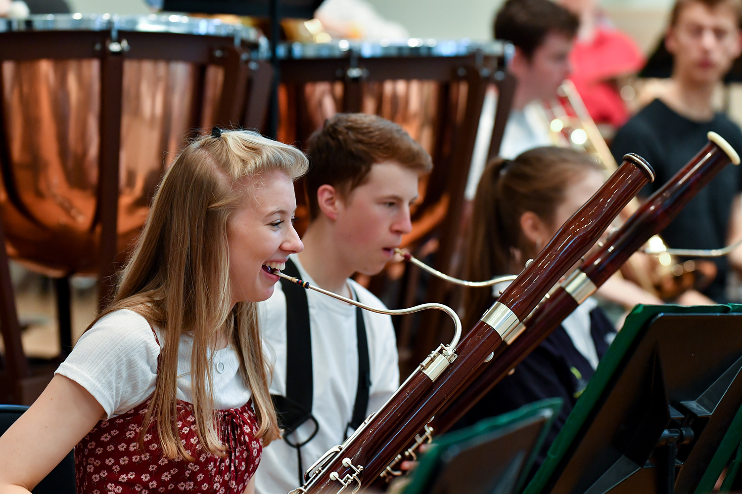 A woman smiles whilst playing the bassoon with another bassoonists playing sitting next to her