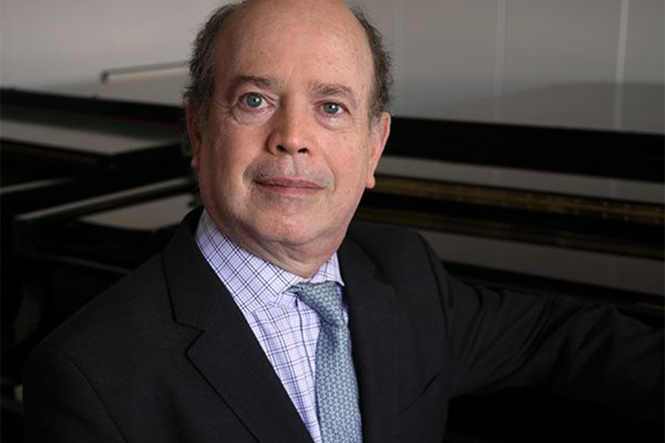 Boaz Sharon wears a suit and tie and sits in front of a piano