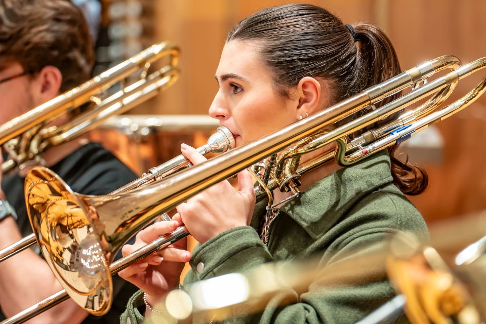 A young woman plays the trombone with an orchestra on stage