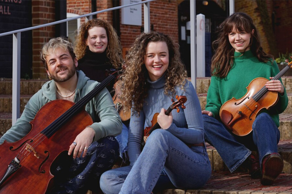 The Calathea Quartet sit on steps outside smiling and holding their instruments