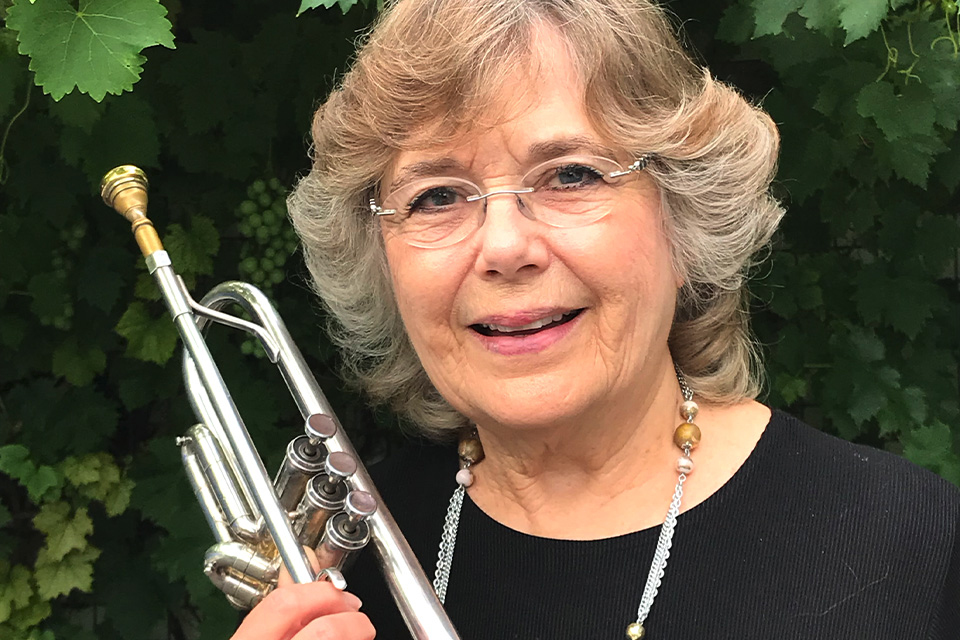 Carole Dawn Reinhart stands outside and holds her trumpet, smiling