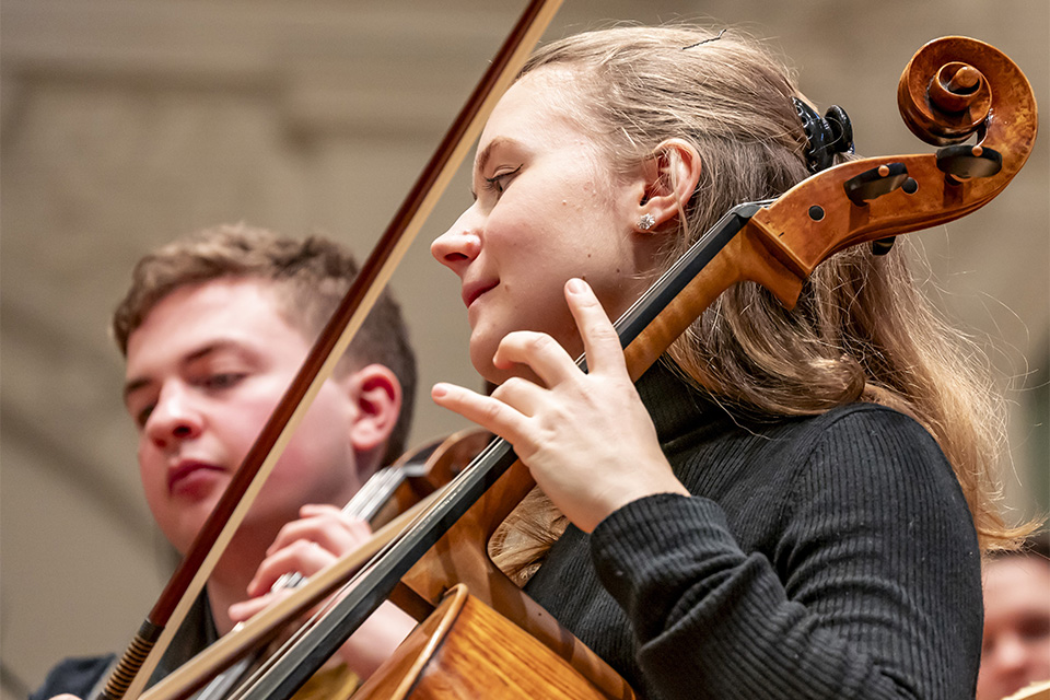 A close up of two cellists who play their instruments on a brightly lit stage