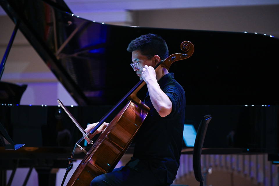 A cellist performs on stage under colourful lights