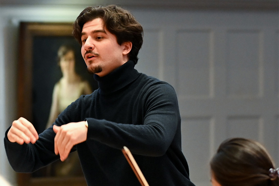 A young man wearss black and conducts with his hands on stage