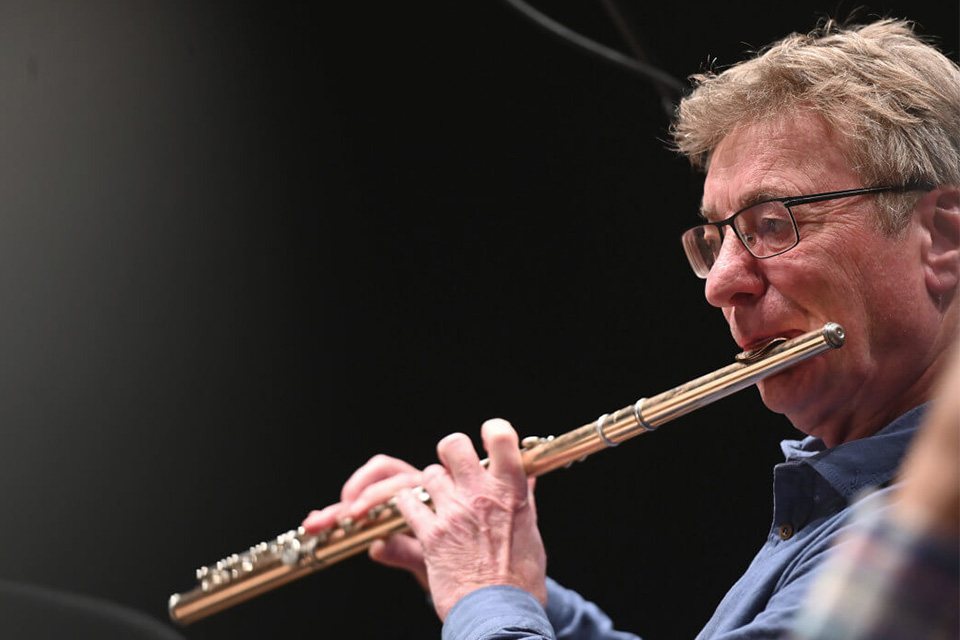 Dietmar Wiesnar wears glasses and looks down as he plays his flute against a dark background