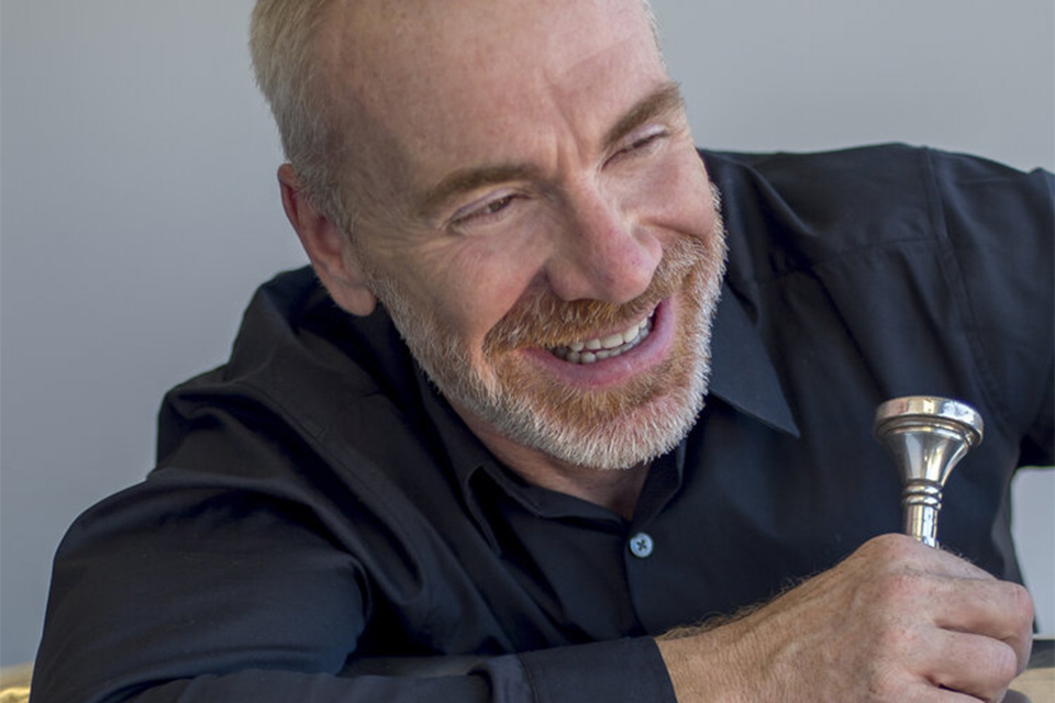 Doug Tournquist wears a black shirt and holds his tuba, laughing