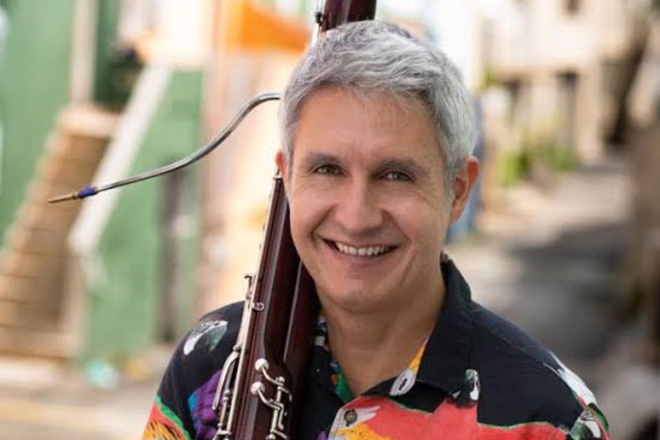 Fábio Cury stands outside with his basoon on his shoulder, smiling broadly