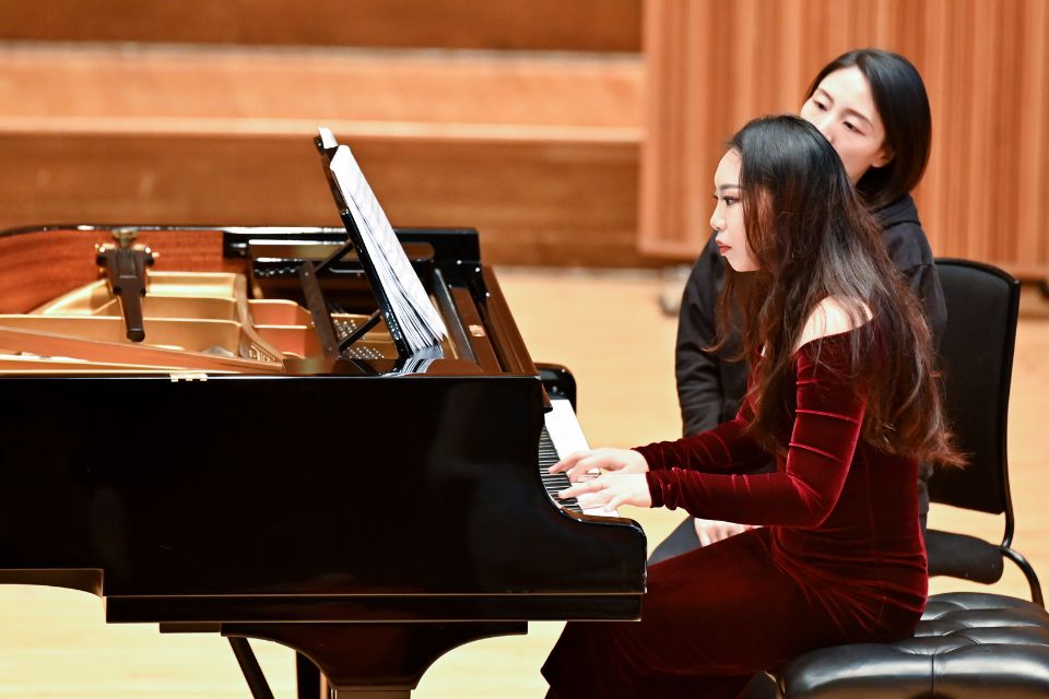 A young woman wears red and plays the piano on stage