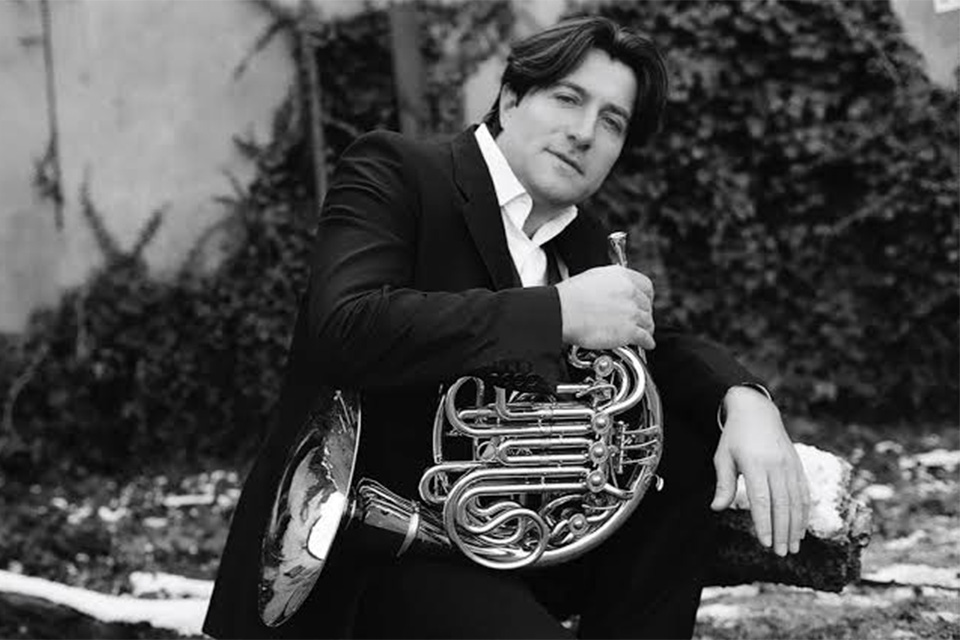 Hervé Joulain wears a suit and holds his horn in a black and white photo