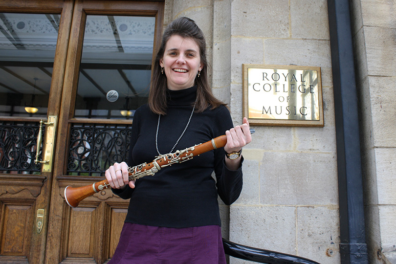 A woman smiling and holding a clarinet, standing in front of the Royal College of Music 