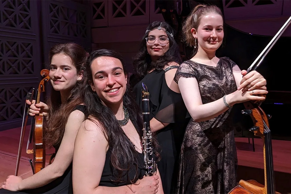 The four members of the Iridescence Ensemble wear black and stand on a stage, smiling