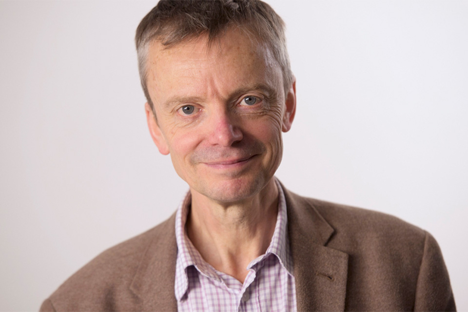 Ivan Hewett wears a shirt and blazer and smiles softly at the camera