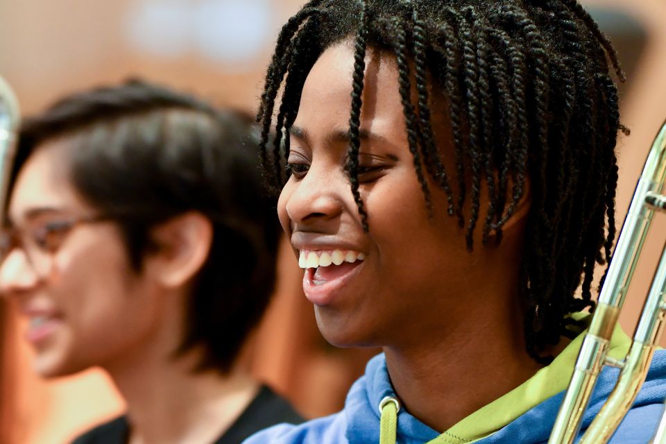 A young young boy holds his trombone and laughs