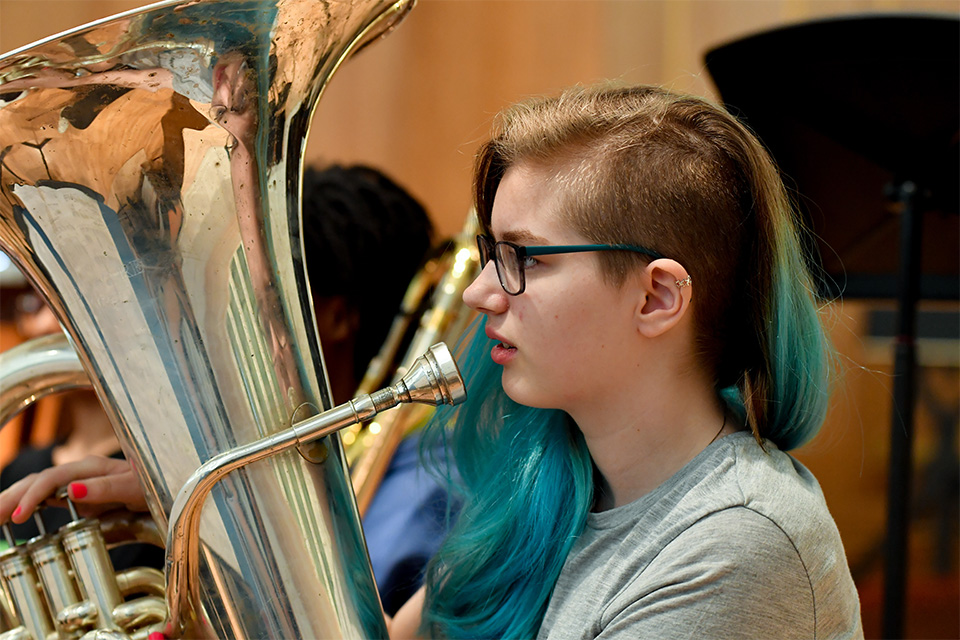 A young girl with blue hair plays the tuba