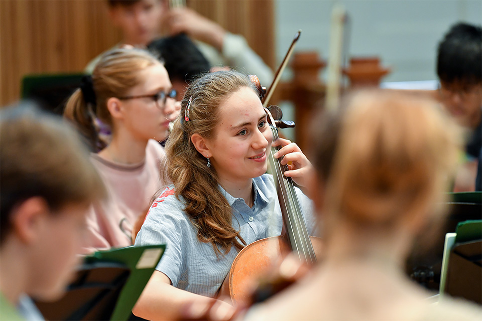 A young girl in an orchestra plays the cello and smiles