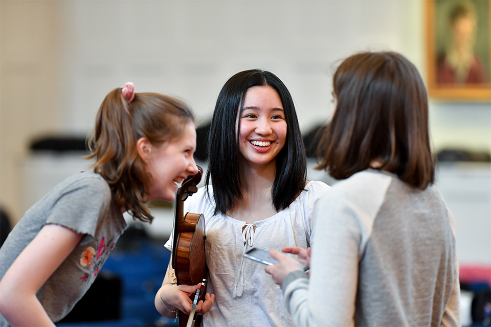 A group of young people hold their instruments as they chat, smiling