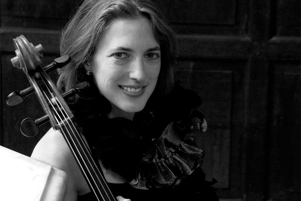 A black and white photo in which Jennifer Morches holds her cello and smiles