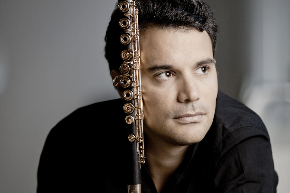 Julien, wearing a black shirt, holds his flute and gazes to his left