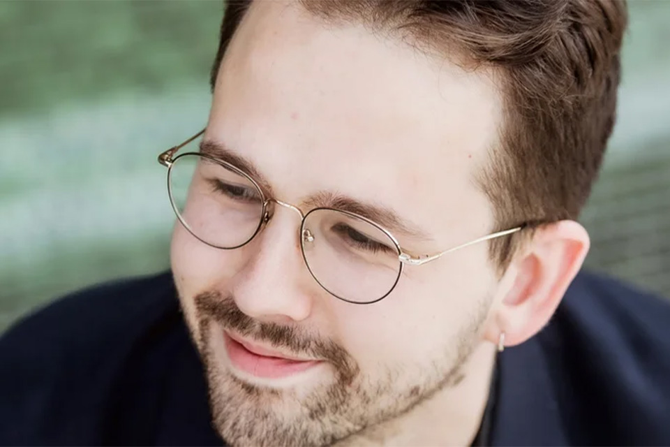 Louis-Victor Bak wears glasses and looks down to his right, smiling softly