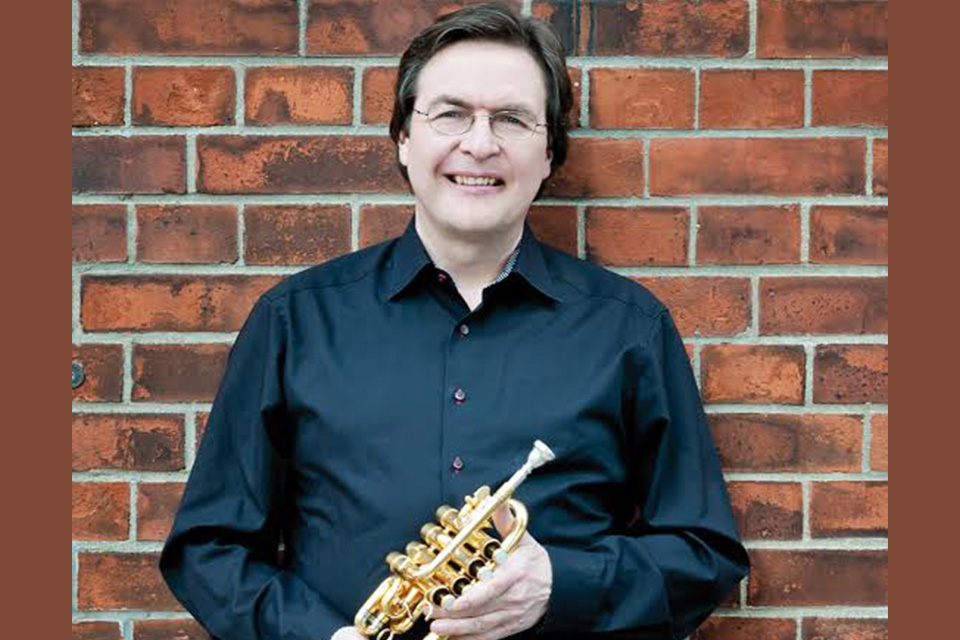 Matthias Höfs wears a black shirt and holds his trumpet, smiling