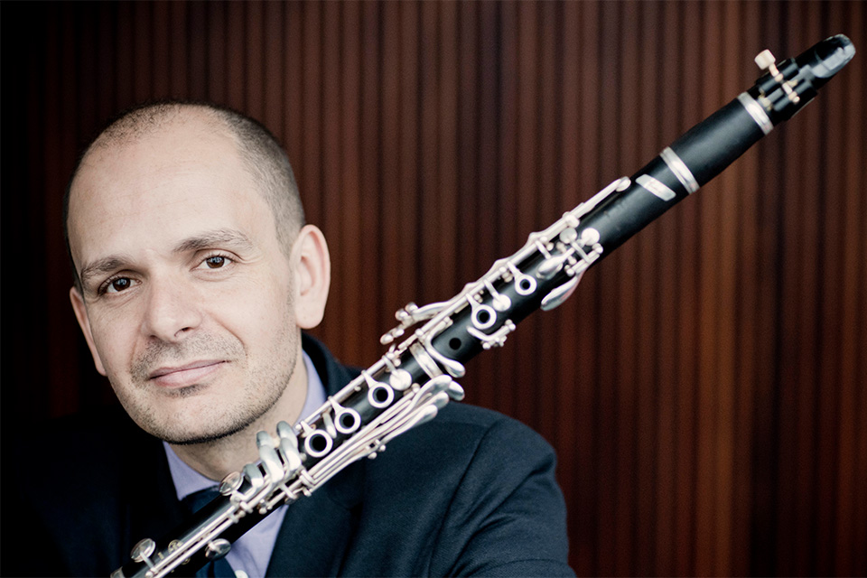 Maximilliano Martín wears a shirt and blazer and rests his clarinet on his shoulder, smiling