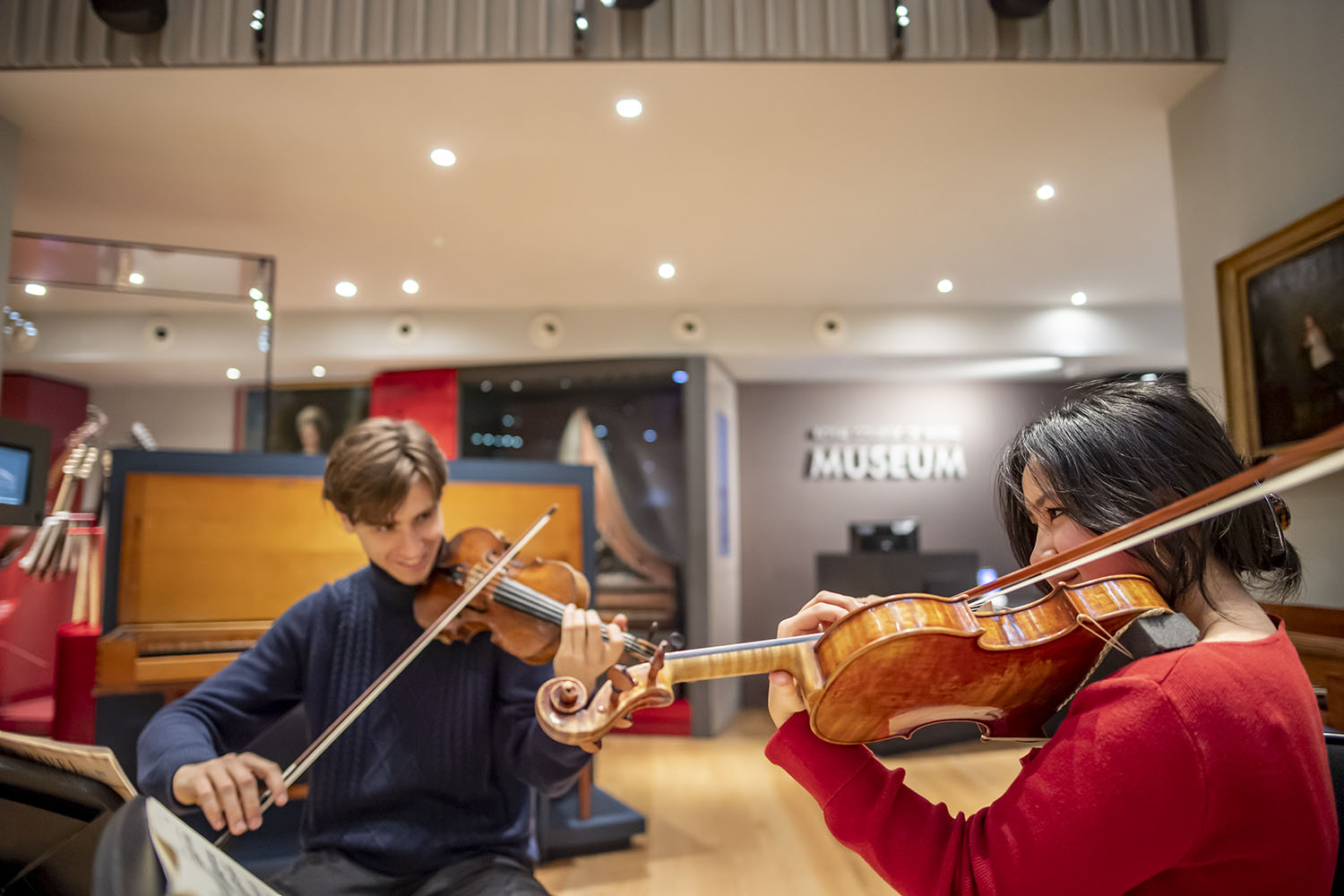 Two violinists sitting down and performing in the Royal College of Music Museum