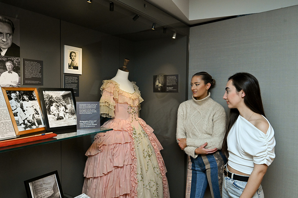 Vistors look at a pink 20th century dress in a museum display case