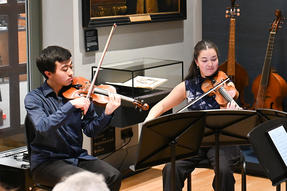 Two violinists wear blue and perform in the RCM Museum