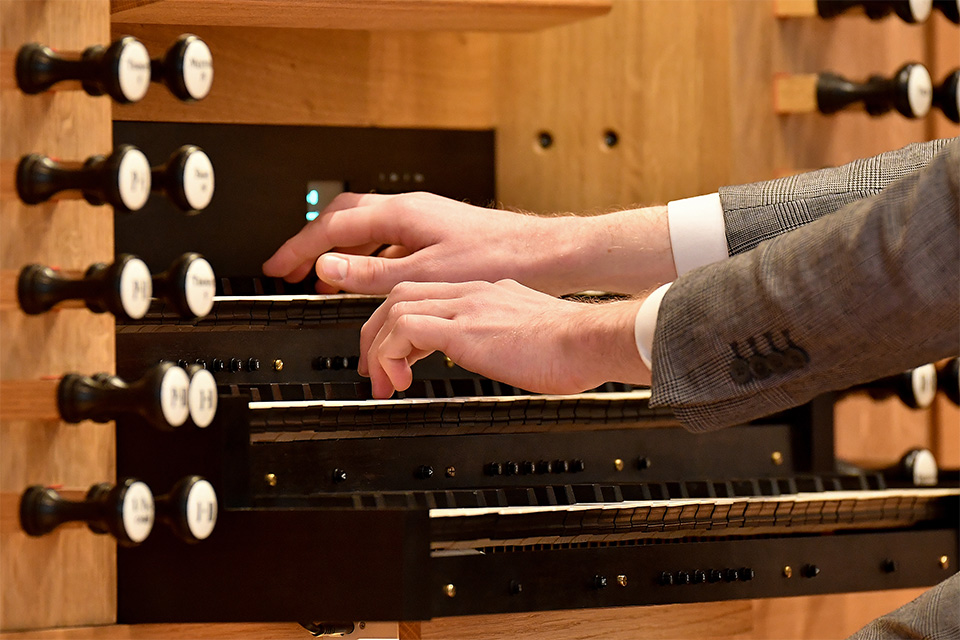 A close-up view of two hands playing the organ, one on top of the other