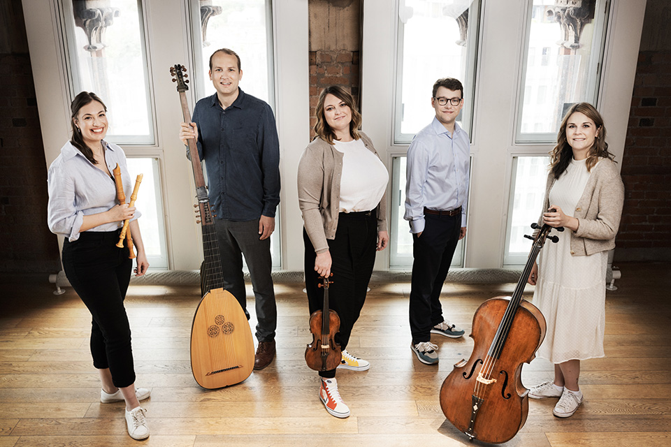 Ensemble Augelletti stand in a brightly lit room in shades of blue and beige, holding their instruments and smiling