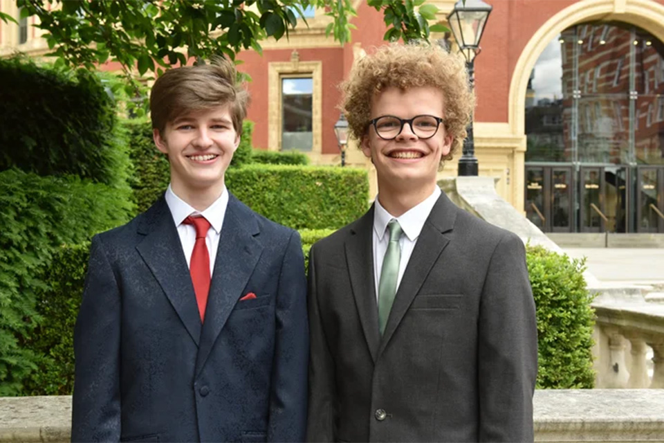 Two teenage boys, Peter Ryan and Finn Kjaergaard, stand outside the Royal College of Music in suits, smiling