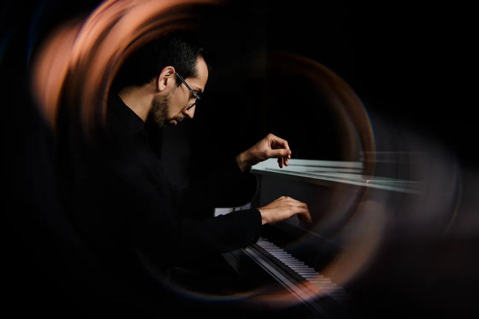 Rishi Mirchandani plays the piano in a dark room as colours swirl around him