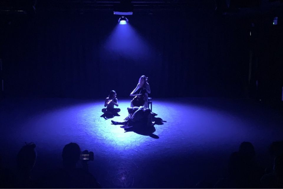 A cellist plays in a dark room under a blue spotlight