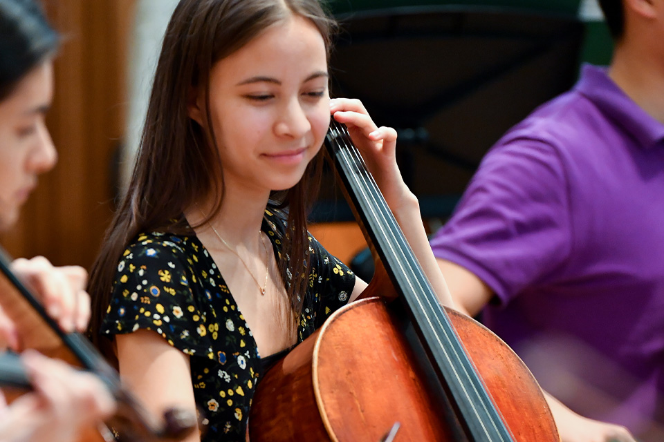 A young girl plays the cello, smiling