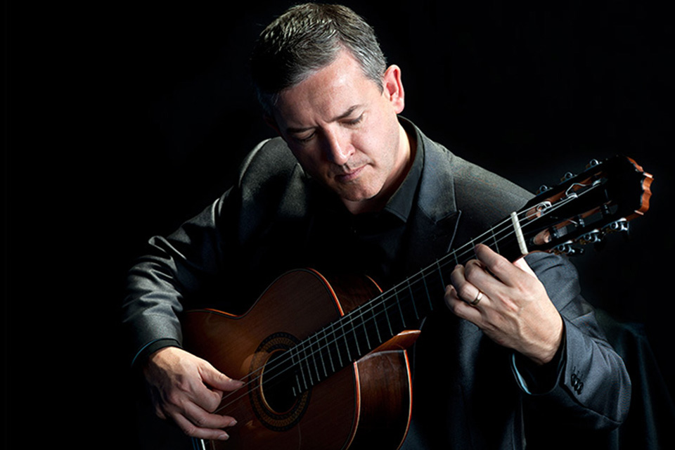 Gary Ryan wears a black shirt and looks down as he plays his guitar