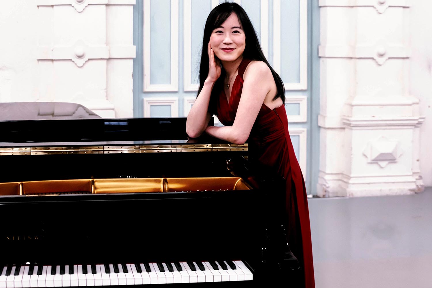 A woman wearing a red dress stands by a piano smiling