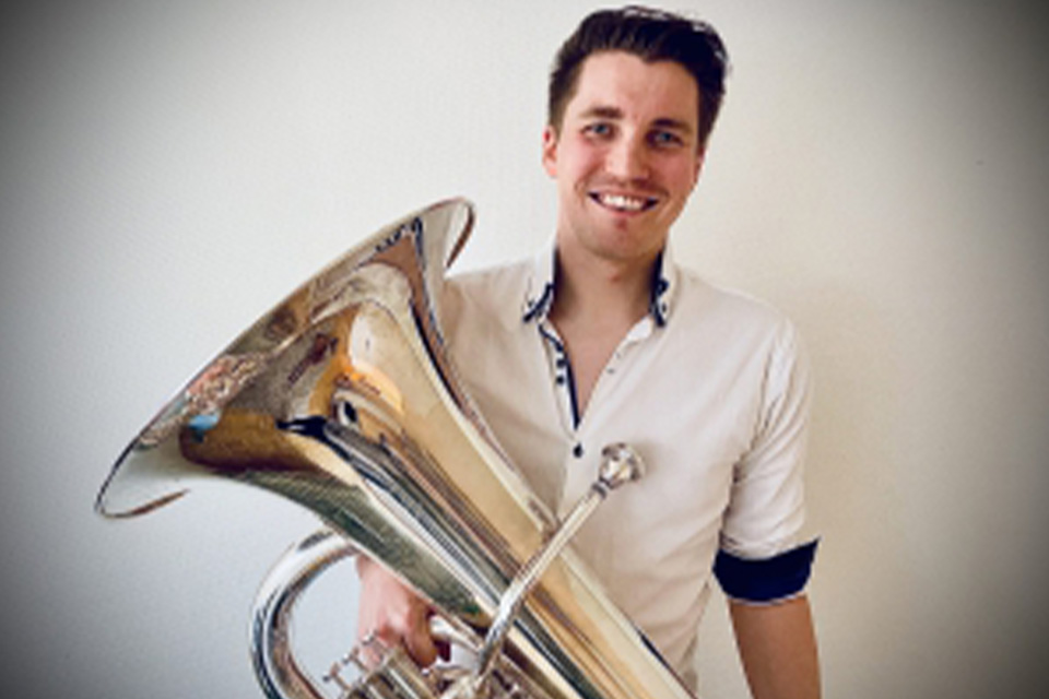 Ross Night wears a white shirt and holds his tuba, smiling broadly